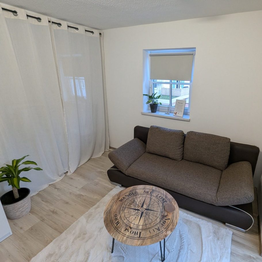 Heller Beratungsraum mit einladendem Ambiete bestehend aus brauner Couch, weißem Teppich, Beistelltisch und Zimmerpflanzen