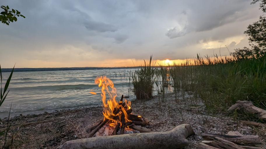 Lagerfeuer am Ufer eines ruhigen Sees bei Sonnenuntergang. Ein Symbol für Geborgenheit und Harmonie