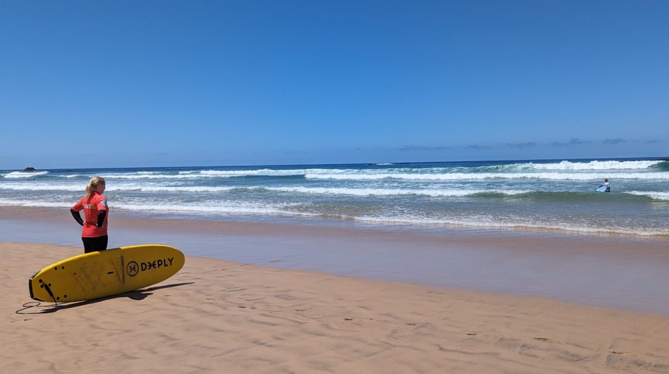 Surferin mit Surfbrett blickt am Strand auf die Wellen hinaus. Ein Symbol für Abenteuerlust