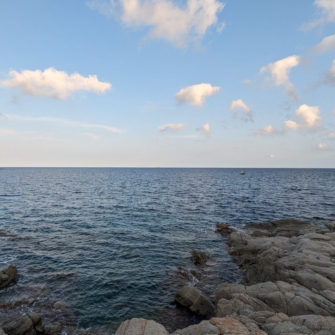 Blick von einer Steinküste aufs ruhige Meer bei sonnigem Wetter. Symbol für Leichtigkeit, Freiheit und Weite.